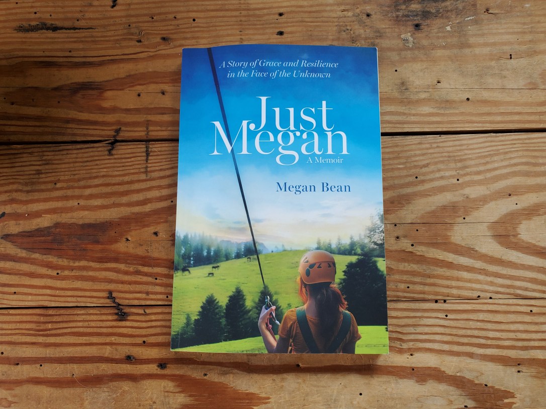 A paperback copy of Megan Bean’s memoir, Just Megan: A Story of Grace and Resilience in the Face of the Unknown, rests on a rustic wooden table.